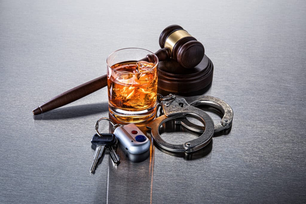 A judge's gavel behind a glass of alcohol and handcuffs